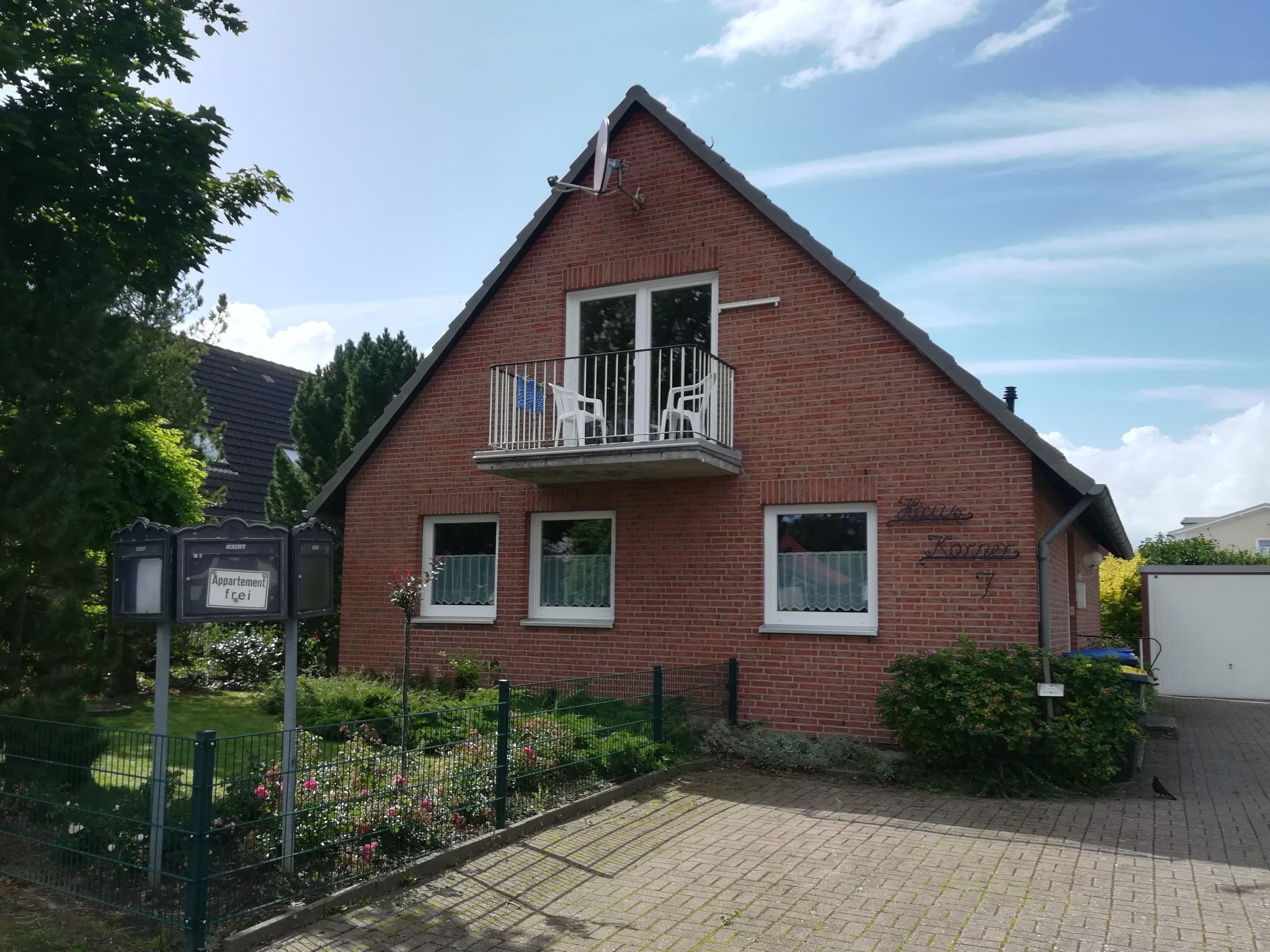 Una casa in mattoni rossi con un balcone, un piccolo giardino e un cartello che indica che si tratta di un appartamento.