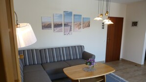 A living room with a sofa, a coffee table with a vase of flowers, and wall art. - Körner Kornhof 7 EG by Interhome (Dahme)