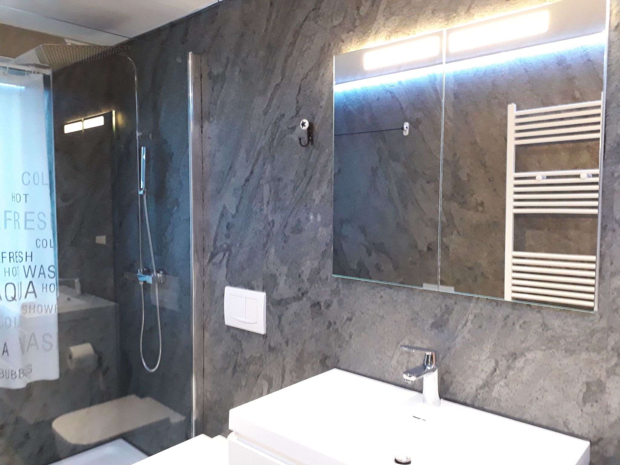 Een moderne badkamer met een douchecabine van glas, een witte wastafel en een spiegel met ingebouwde handdoekhouders.