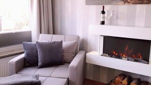 A modern living room with a sofa, a fireplace, a painting, and a window with curtains. - Strandappartment by Interhome (Glücksburg)