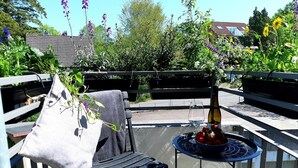 A balcony with a chair, a table with a bottle and glasses, and a view of a garden and buildings. - Strandappartment by Interhome (Glücksburg)