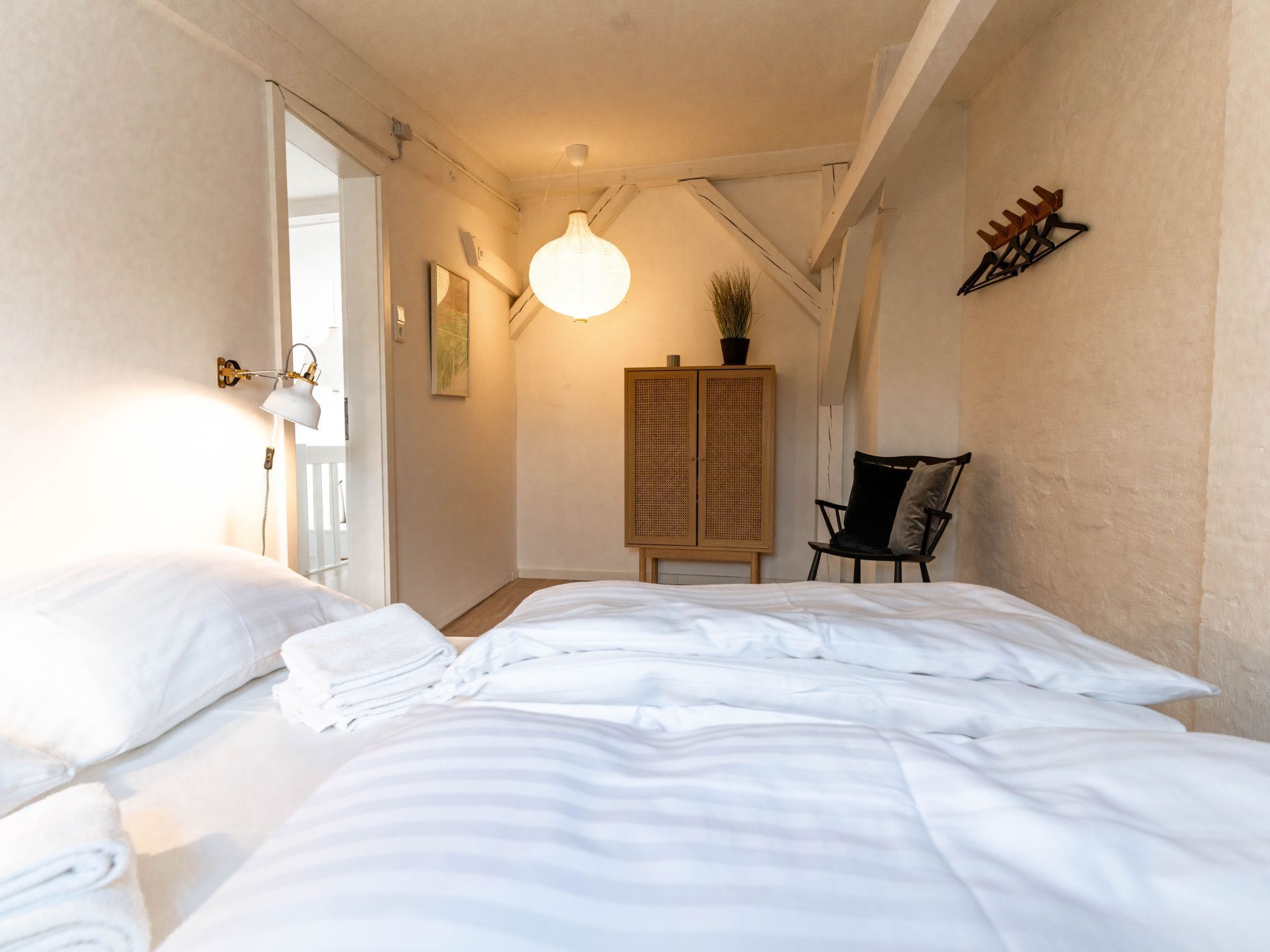A bedroom with two beds, a rattan cabinet, a chair, and a hanging light fixture.