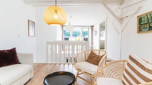 A bright living room with a white sofa, a wicker chair, a black coffee table, and a hanging lamp. - Himmelskoje mit Große Dachterrasse & Hafenblick by Interhome (Altstadt)