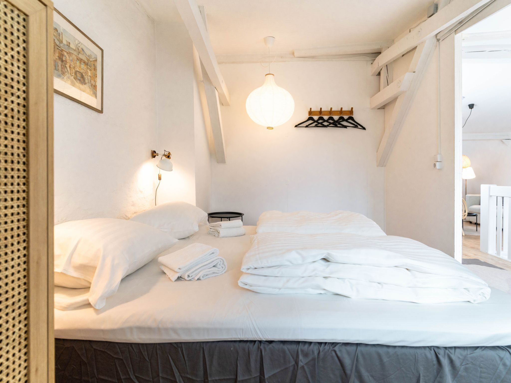 Ein ordentlich bezogenes Bett mit weißen Bettwäsche, einer Nachttischlampe und einem gerahmten Bild an der Wand.
