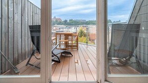 A wooden deck with a table and chairs, a metal chair, and a view of buildings and trees through a glass door. - Himmelskoje mit Große Dachterrasse & Hafenblick by Interhome (Altstadt)
