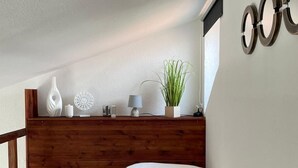 Ein Schlafzimmer mit einem Holz-Kopfteil, einem Bett mit brauner Decke, einer kleinen Topfpflanze und einem Wandspiegel.