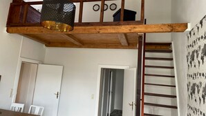 Ein Loft-Zimmer mit Holzbalkendecke, einer Pendelleuchte, einer Treppe und einer Tür zu einem weiteren Raum.