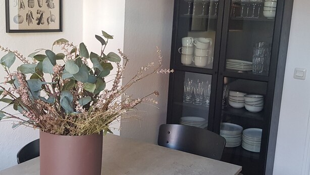Un comedor con una mesa, sillas, una planta en maceta y un aparador con vajilla y copas.