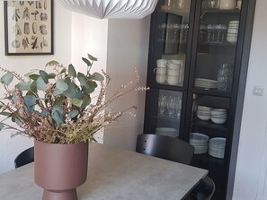 Ein Essbereich mit Tisch, Stühlen, einem Blumentopf und einem Schrank mit Geschirr und Gläsern.