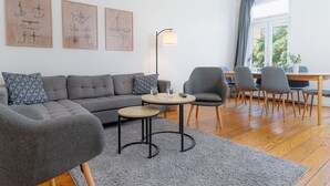 A modern living room with a grey sofa, a round coffee table, and grey armchairs. There are framed technical drawings on the wall, a floor lamp, and a window with curtains. - Koje Marina by Interhome (Altstadt)