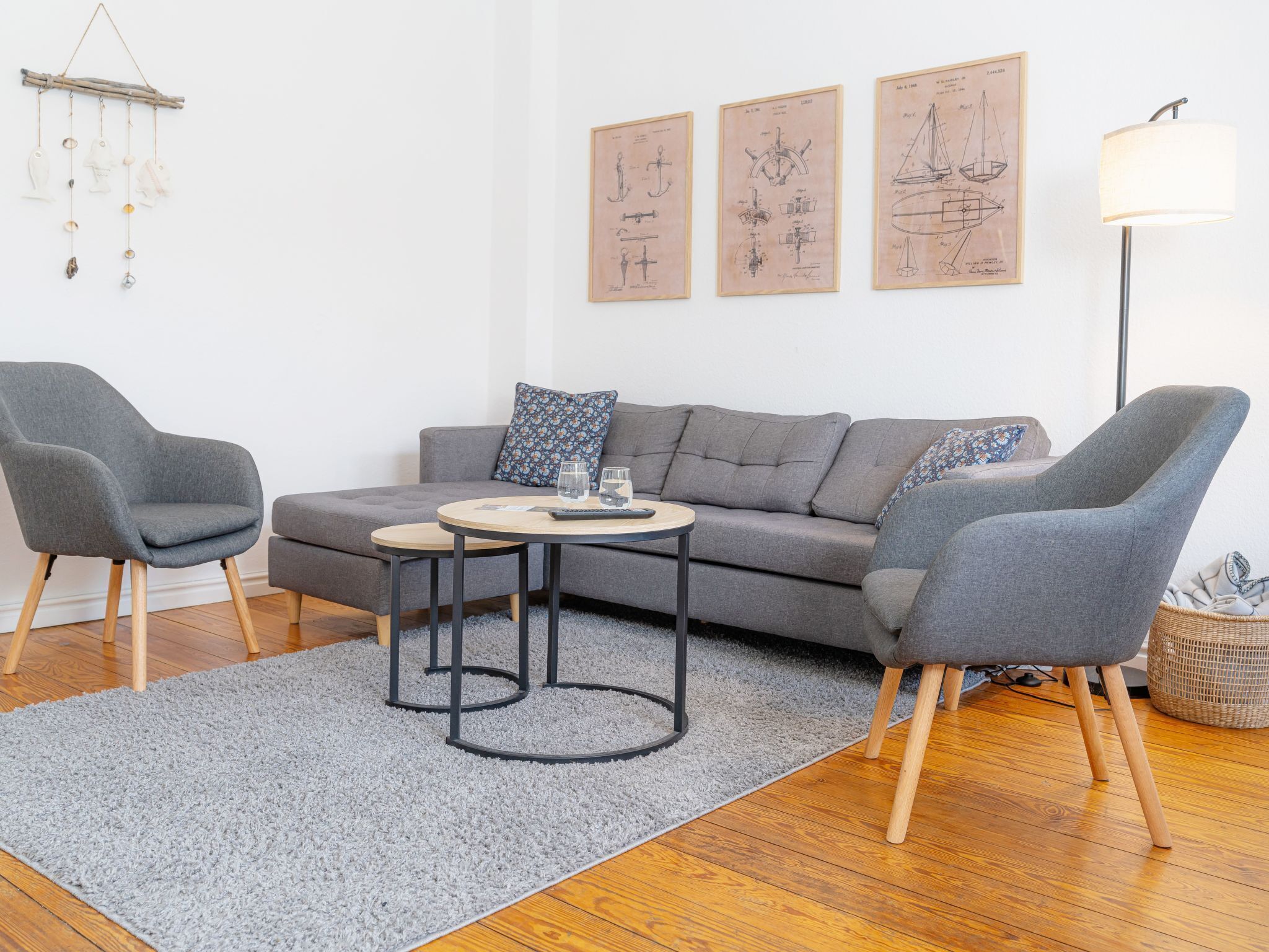 Una sala de estar moderna con un sofá gris, dos sillones, una mesa de centro redonda y una alfombra gris. Hay tres dibujos enmarcados en la pared.