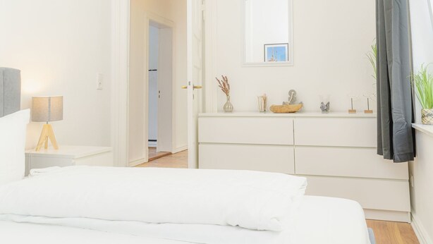 A hotel room with a bed, a bedside table with a lamp, a dresser, and a mirror. - Koje Marina by Interhome (Altstadt)