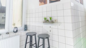 A kitchen with white tiles, two black stools, a window, and a shelf with plants. - Koje Marina by Interhome (Altstadt)