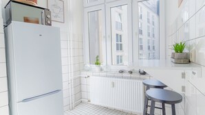 A modern kitchen with white tiles, a white refrigerator, a window with a view of buildings, and a small plant on the counter. - Koje Marina by Interhome (Altstadt)