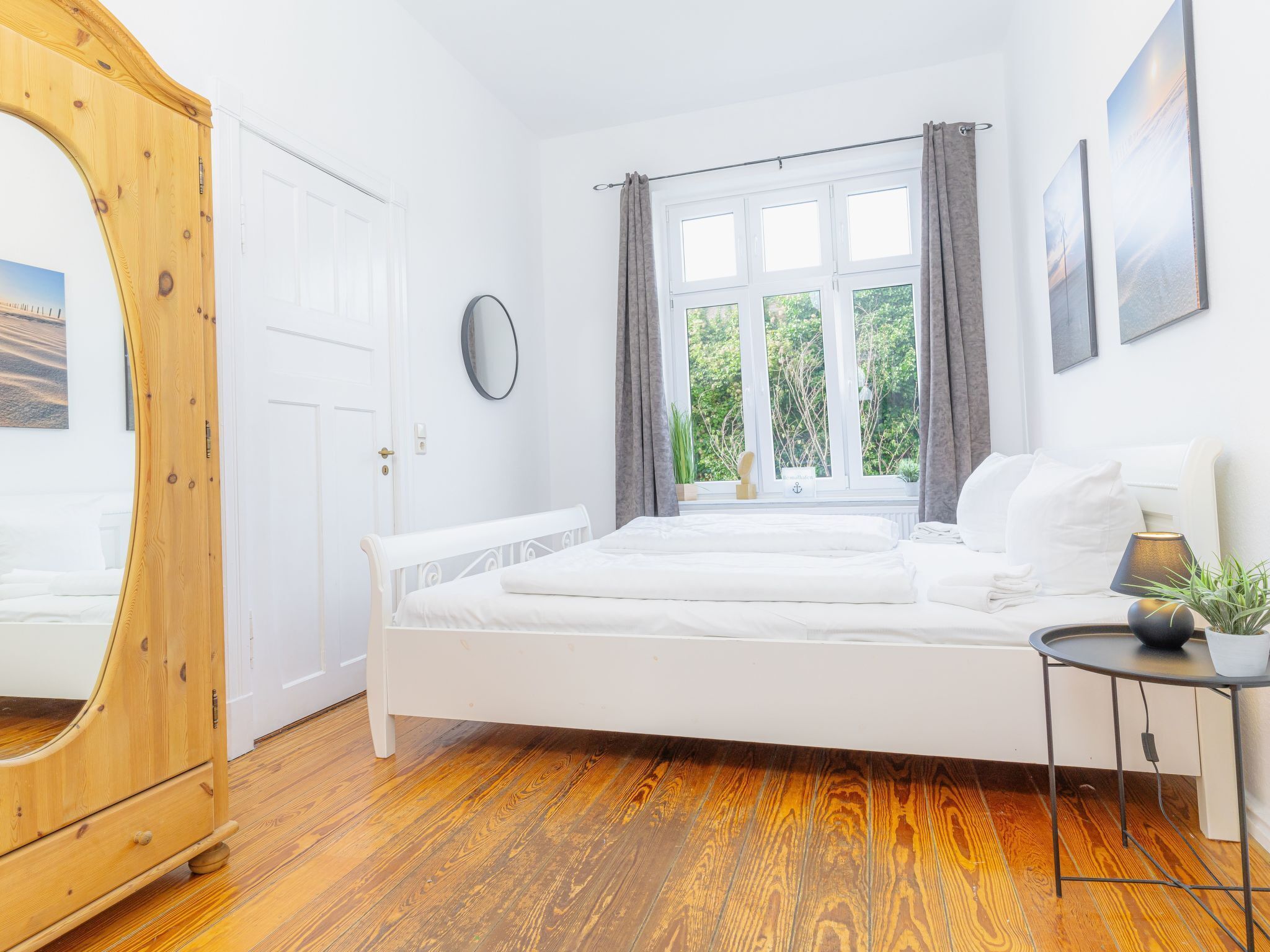 Un dormitorio con un armario de madera, una cama, una mesita de noche con lámpara y una ventana con cortinas.