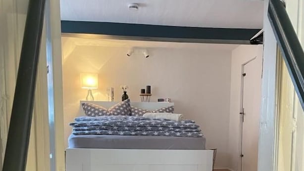 Una camera da letto con un letto, un comodino, una lampada e una porta che dà su un'altra stanza.