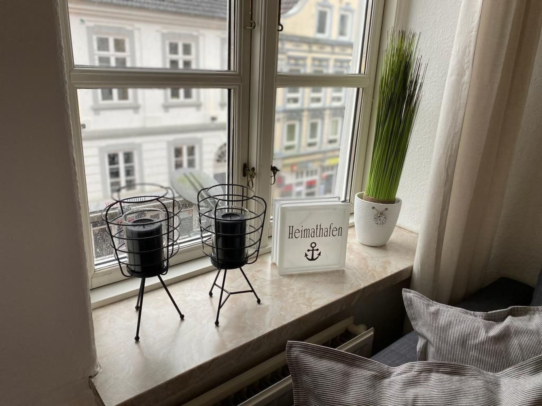 A window with two black candle holders, a potted plant, and a sign with "Heimhafen" written on it.