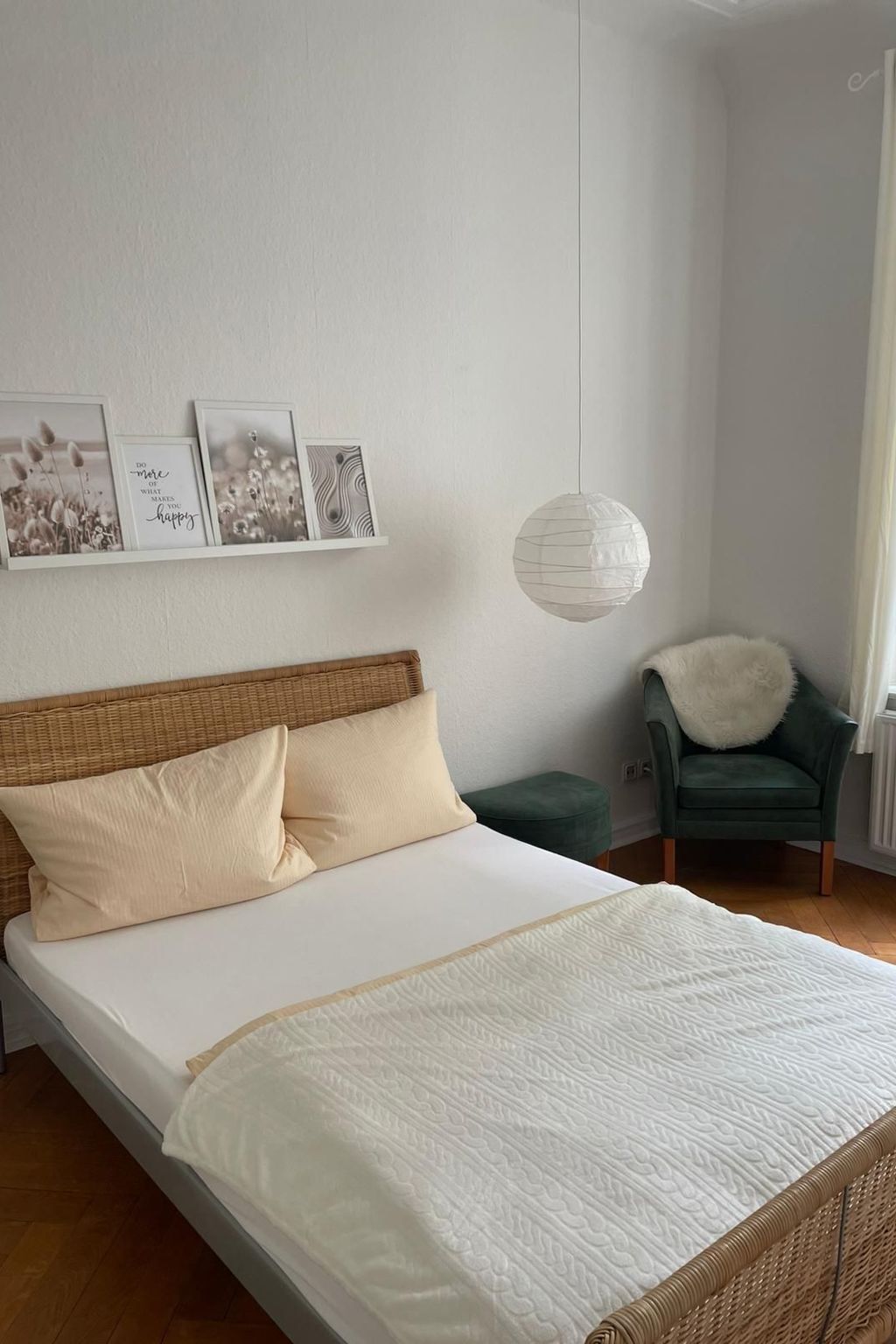A bedroom with a bed, a wicker headboard, a green chair, and a white hanging light fixture.