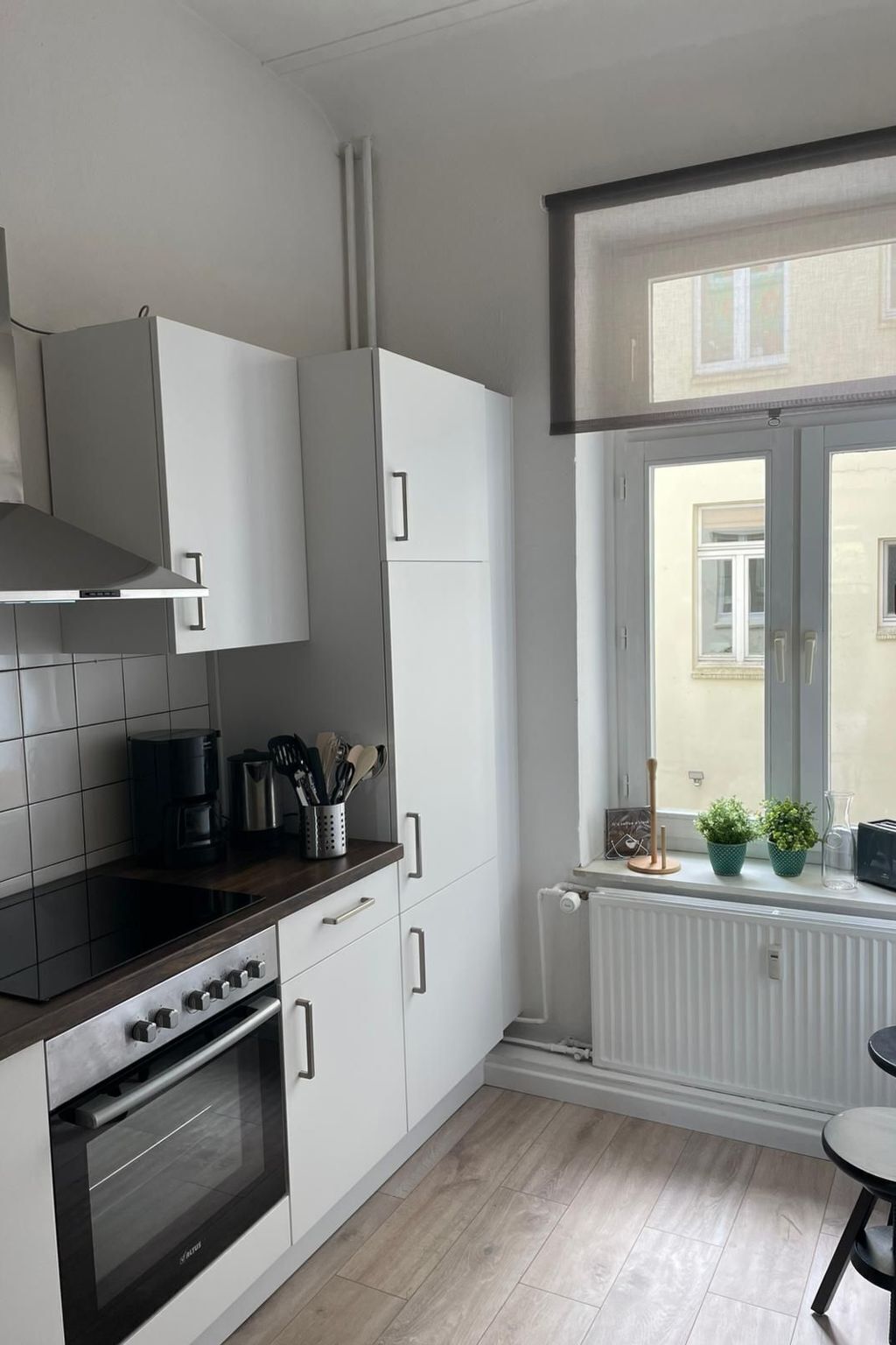 Eine moderne Küche mit weißen Schränken, einer schwarzen Arbeitsplatte und einem eingebauten Backofen. Ein Fenster bietet Blick auf ein Gebäude.
