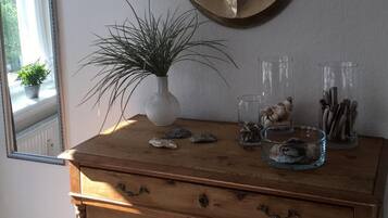 Une commode en bois avec des tiroirs, une ancre décorative accrochée au mur, une plante en pot et un vase en verre contenant des coquillages.