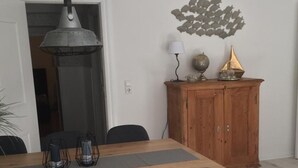 A dining area with a wooden table, four grey chairs, a hanging lamp, a wooden cabinet with decorative items, and a wall art piece. - Admiralskoje by Interhome (Altstadt)