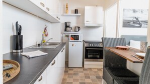 Ett kompakt kök med mikrovågsugn, spis och kaffebryggare. Här finns också ett litet kylskåp, en diskho och en stol av rotting.