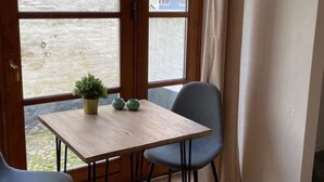 Quarto com mesa de madeira e duas cadeiras, relógio na parede e janela com cortinas.
