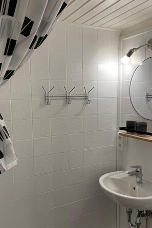 Een badkamer met witte betegelde wanden, een wastafel met spiegel en een douche.