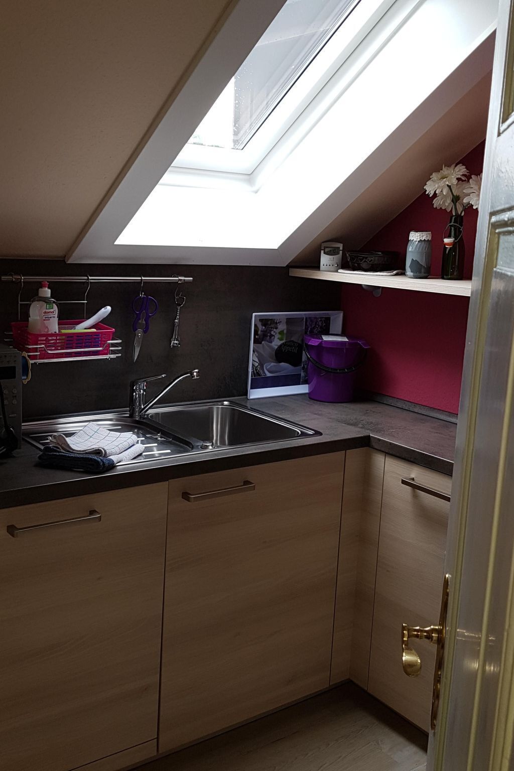 A kitchen with a skylight, wooden cabinets, a sink, and various kitchen utensils.
