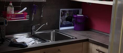 A kitchen with a skylight, wooden cabinets, a sink, and various kitchen utensils.