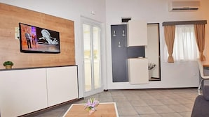 A modern living room with a flat-screen TV, a wooden accent wall, a sliding door, a small plant, a coffee table with flowers, and a sofa. - Modernes und komfortables Wohndesign by Interhome (Medulin)