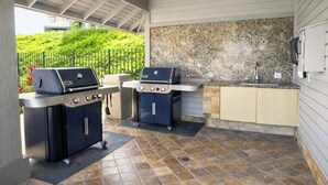 Een buitenkeuken met twee barbecues, een spoelbak en een steen achterwand.