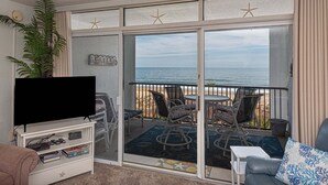 A balcony with a TV, seating, and a view of the ocean.