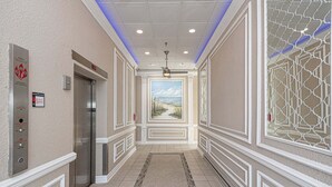 A hallway with an elevator, a patterned rug, and a decorative wall with a view of the beach.