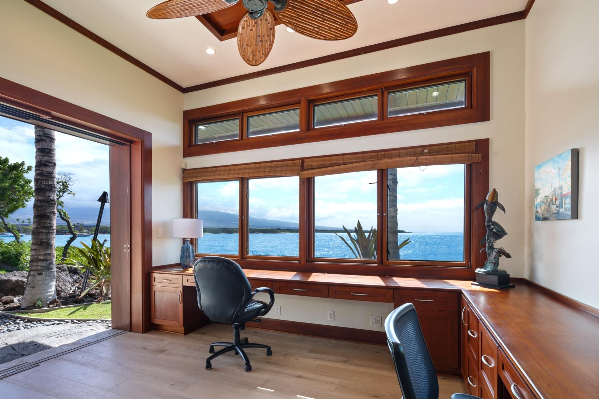 A spacious room with large windows, a desk, two chairs, a ceiling fan, and a view of the sea.
