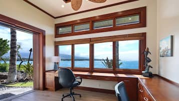 A spacious room with large windows, a desk, two chairs, a ceiling fan, and a view of the sea.