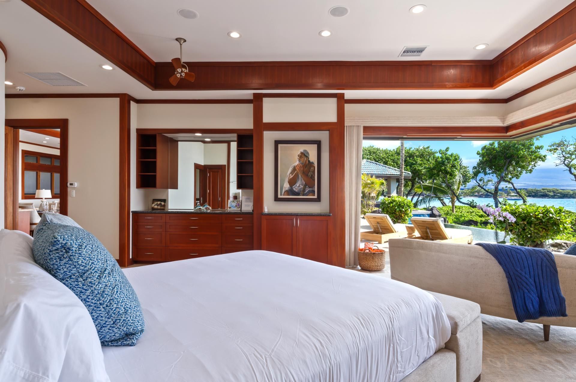 Un dormitorio con una cama grande, un aparador, un espejo y vistas a una piscina y al océano.