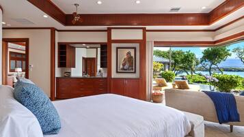 Un dormitorio con una cama grande, un aparador, un espejo y vistas a una piscina y al océano.