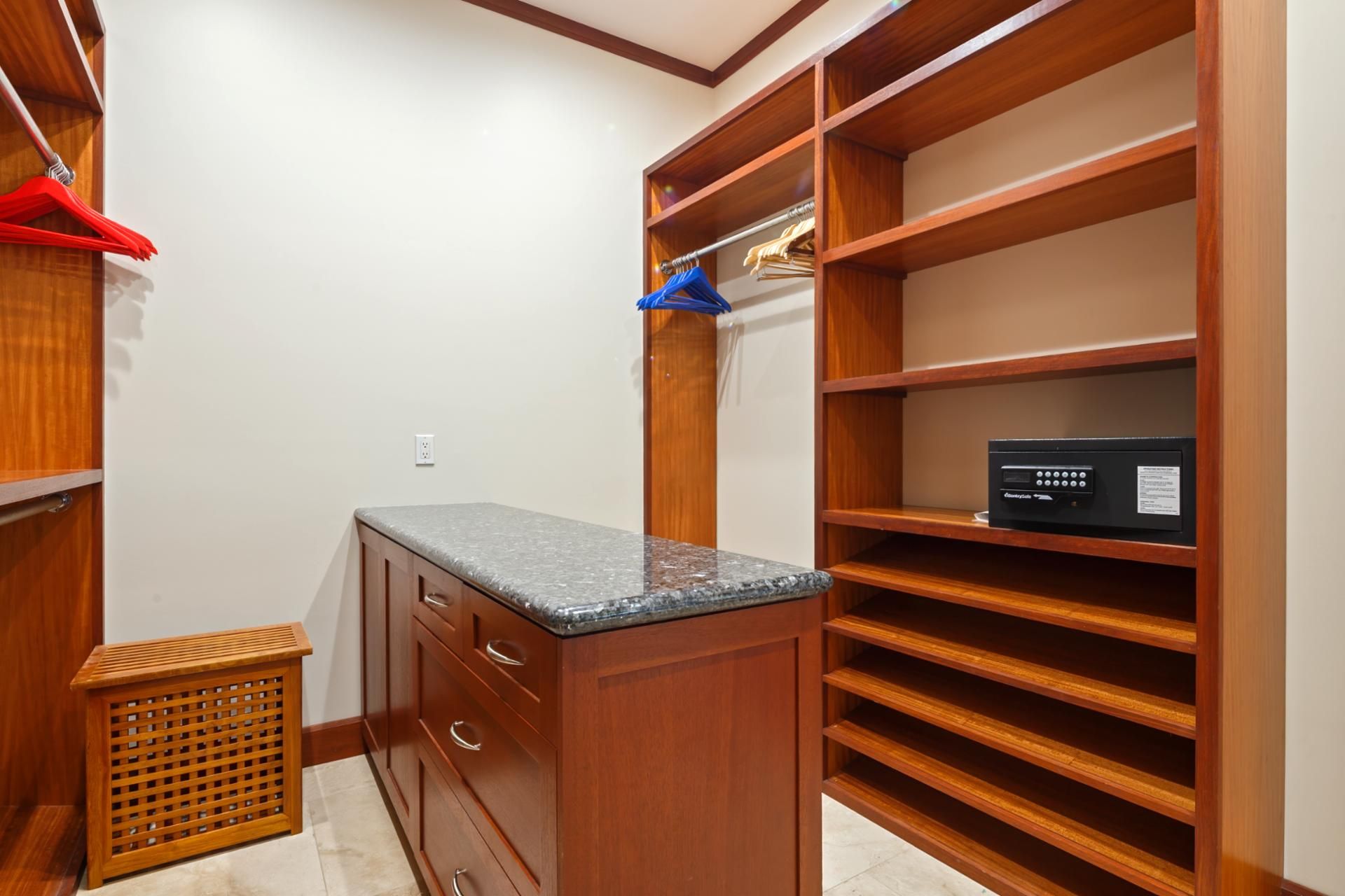 A walk-in closet with wooden shelving, a granite countertop, and a small trash bin.