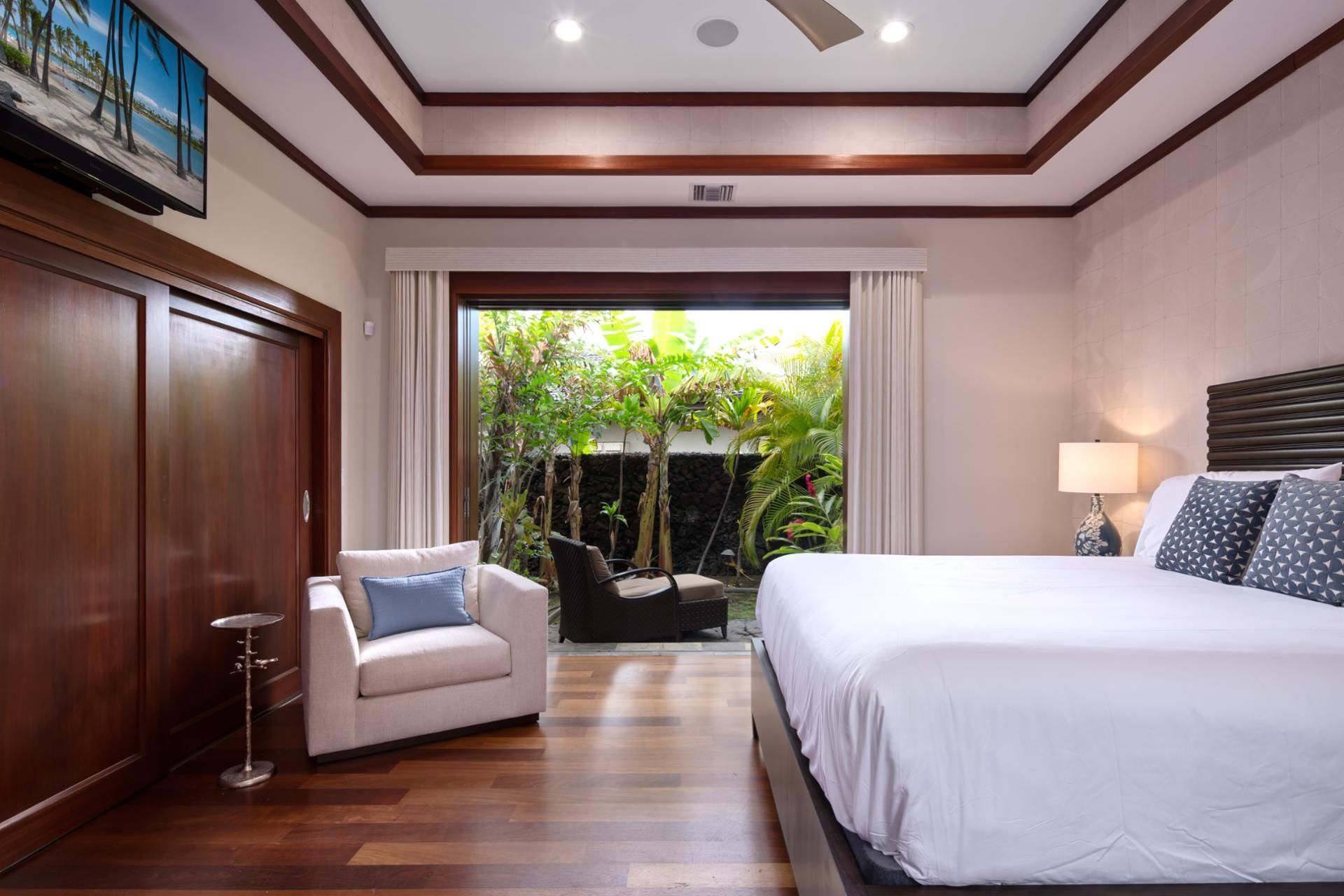 A hotel room with a bed, a chair, a TV, and a view of greenery outside.