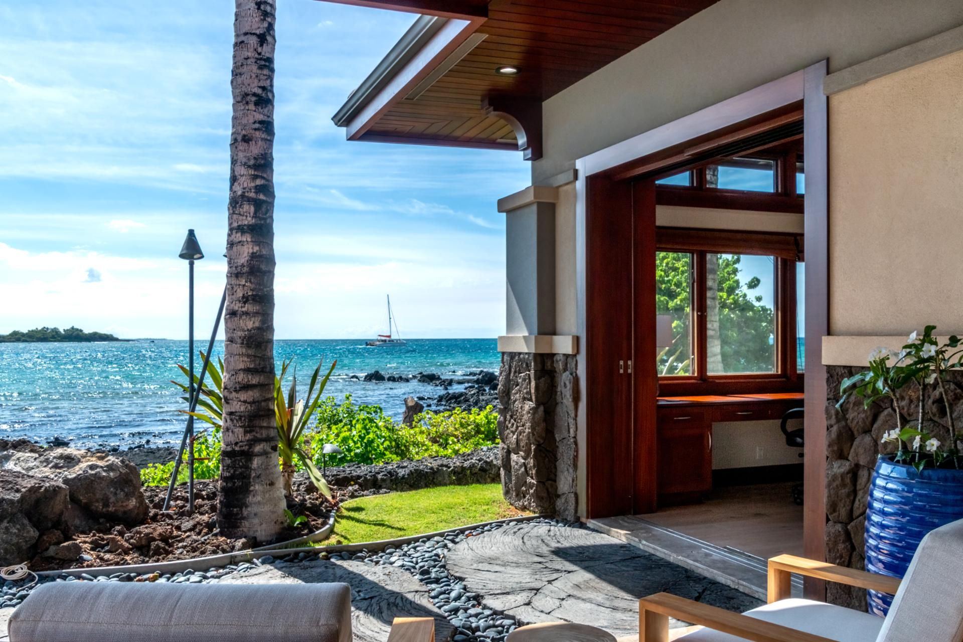 A modern house with a stone exterior, a wooden deck, and a view of the ocean.