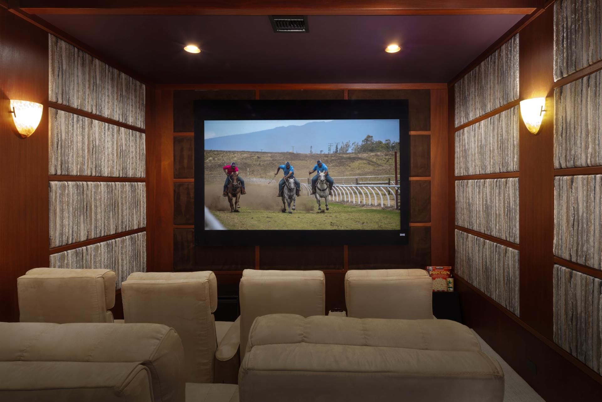 A cinema room with a large screen, comfortable seating, and wooden paneling.