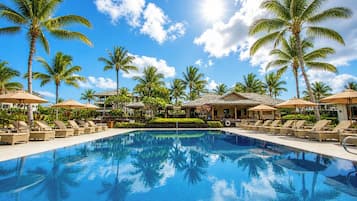 A pool with lounge chairs and umbrellas, surrounded by palm trees and a building with a tiled roof.