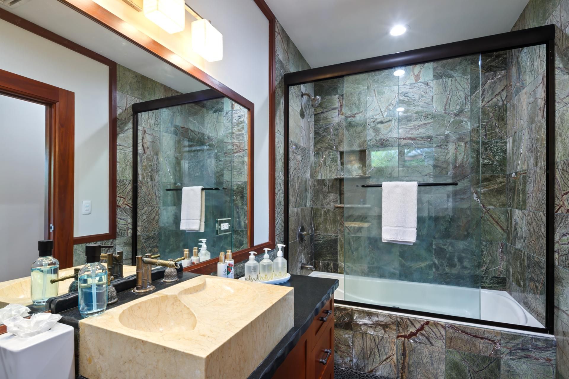 A bathroom with a marble sink, a large mirror, and a glass-enclosed shower.