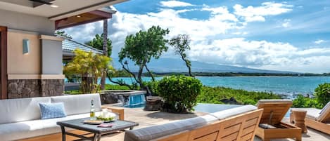 A modern outdoor seating area with a view of the ocean, a stone wall, and a wooden ceiling.