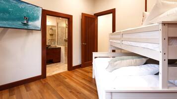 A room with a bunk bed, wooden flooring, a bathroom with a glass shower, and a painting of a surfer on a wave.