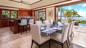 A dining area with a view of the ocean, a kitchen with wooden cabinets, and a ceiling fan.