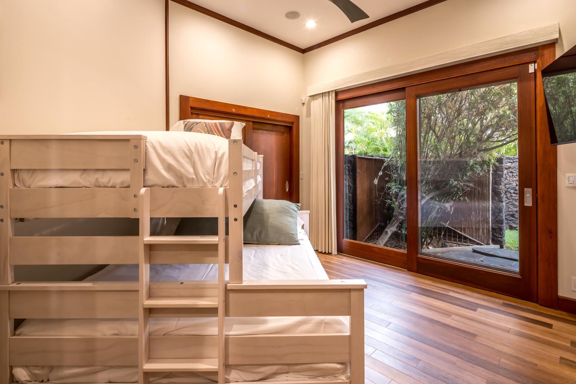 A room with a bunk bed, a sliding glass door to a garden, and a wooden floor.
