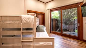 A room with a bunk bed, a sliding glass door to a garden, and a wooden floor.