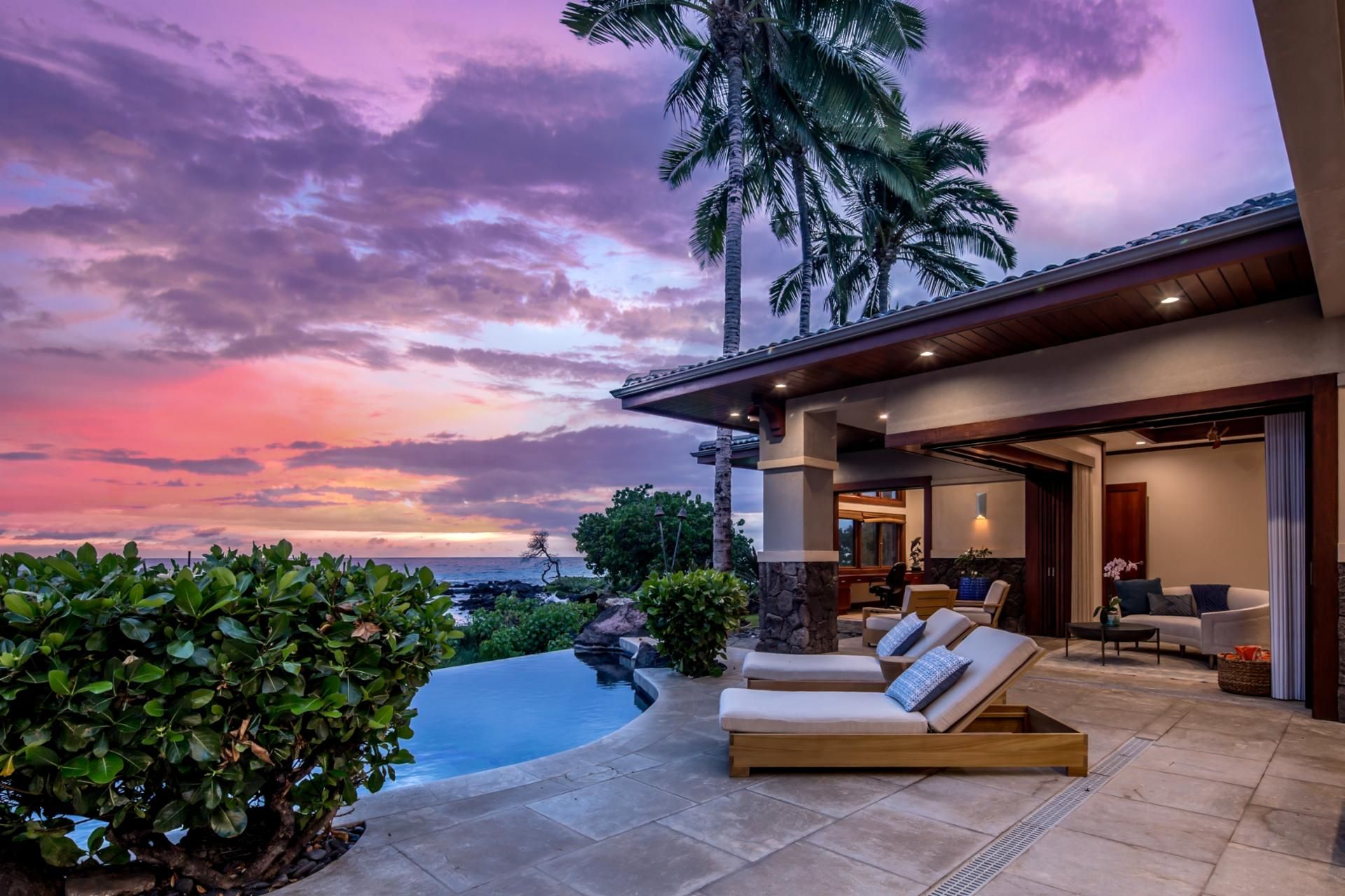 A modern house with a pool, outdoor seating, and a view of the ocean at sunset.